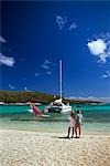 COUPLE STANDING ON BEACH WATCHING A SAILBOARDER AND A CATAMARAN TOBAGO CAYS, WEST INDIES