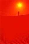 MAN WALKING ALONE DESERT SAND DUNE UNDER RED SKY AND YELLOW SUN