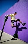 1990s YOUNG MAN WITH ROLLER BLADES JUMPING AGAINST PURPLE WALL