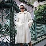 1960s WOMAN WEARING WHITE MINK FUR COAT HAT SUNGLASSES BY WROUGHT IRON GATE