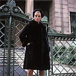 1960s YOUNG WOMAN WEARING DARK MINK COAT HAT STANDING ORNATE WROUGHT IRON GATE FUR