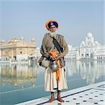 Sikh man in traditional clothing standing near a pond with a temple in the background, Golden Temple, Amritsar, Punjab, India