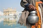 Homme tenant un kamandal avec un temple dans le fond, le Temple d'or, Amritsar, Punjab, Inde