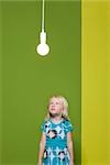 Little girl staring up at illuminated light bulb suspended overhead