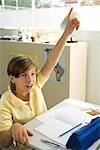 Boy sitting in classroom, raising hand enthusiastically