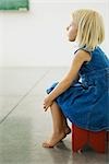 Little girl sitting on stool, looking away in thought