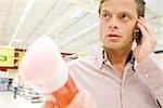 Man in supermarket using cell phone, choosing bottle of shower gel