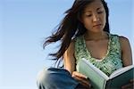 Woman reading book outdoors, hair blowing in breeze