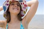 Jeune femme portant un chapeau de soleil à la plage, en levant et souriant