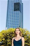 Woman in tank top looking away, high rise building in background