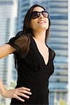 Woman dressed in black clothing and sunglasses, looking up and smiling