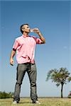 Man standing outdoors drinking from bottle of water, low angle view, full length