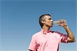 Mann, im freien stehend niedrigen trinken aus einer Flasche Wasser, Winkel Ansicht, blauen Himmel im Hintergrund