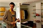 Young man with black hair standing in a clothes shop and is holding a high-heel, selective focus