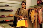 Jeune homme avec des lunettes de soleil et sacs dans sa position de main dans un magasin de vêtements