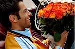 Young man with black hair sitting in a car with a bunch of roses, close-up