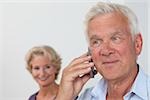 Alter Mann am Telefon mit Frau im Hintergrund