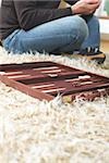 Mann, sitzend Kreuz-beinige auf dem Fußboden und Backgammon-Brett auf einem Teppich verlegen