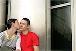 Teenage couple sitting in front of a office building while he kissing her