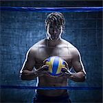 Studio shot of volleyball player standing behind net and holding ball