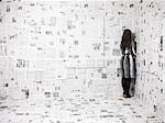 Vue arrière de la jeune femme debout dans le coin de journaux couverts chambre, studio shot