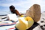 Frau am Strand liegend, mit Buch und Strand-Tasche