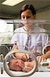 Nurse examining newborn in incubator