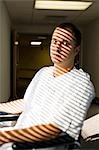 Man in wheelchair sitting in corridor with horizontal blind shadows