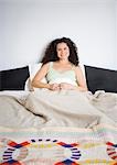 Femme assise dans son lit avec les bras croisés en souriant