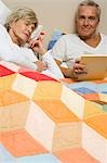 Mature man in bed reading with sleeping woman