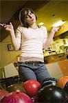 Low angle view of a teenage girl looking at bowling balls and scratching her head