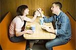 High angle view of a young man and a teenage girl sitting in a restaurant and leaning forward to kiss