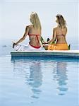 Rear view of a young woman and a mid adult woman sitting in a lotus position at the poolside