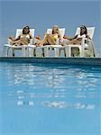 Three young women sunbathing by the pool
