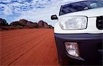 Vehicle on a dirt road through the Outback,with red rocks of The Olgas behind