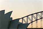 The Sydney Opera House and Harbour Bridge are silhouetted at sunset as a group of climbers scale the arches of the iconic bridge