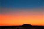 Australie, Northern Territory. Avant le lever du soleil, Uluru ou Ayres Rock est silhouetté sur un magnifique rouge sang à ciel orange. Cette image est extraite de The Olgas, à 16 km de la caractéristique phare.