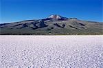 View across the great white expanse that is the Salar de Uyuni,the largest salt flat in the world,towards village of Coquesa and towering above it the extinct volcano,Cerro Tunupa 5432m. The lines on the slopes of Tunupa are drystone walls or pircas.