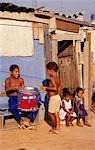 Deux petites filles et deux garçons assis à l'avant de la maison dans une favela à Sao Paulo, à côté d'un tambour.