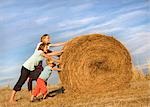 girl, woman, boy pushing hay bale