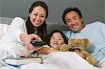 Famille regarder TV ensemble dans son lit, mère à l'aide de la télécommande