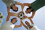 Four women holding soccer ball together, view from below.