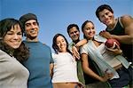 Group of young people outdoors, one young woman holding football, low angle view.