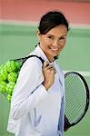 Woman with tennis balls and racket standing on tennis court, portrait