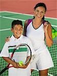 Mother and son by net on tennis court, portrait, high angle view