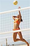 Female beach volleyball player jumping to spike volleyball over net