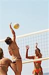 Beach volleyball player jumping to spike volleyball over net, opponent defending
