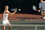 Tennis Player Swinging at Ball near tennis net; doubles partner squatting behind