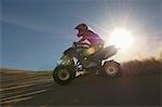 Man riding quad bike in desert against sun