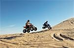 Men doing wheelies on quad bikes in desert